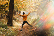 Boy Leaping In The Air On Path Under Tree With Rainbow Light Flare