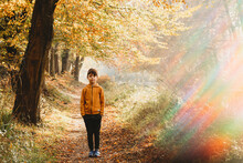 Boy Standing On Path Under Tree With Rainbow Light Flare