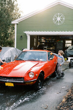 Little Boy In Sweater Washing A Classic Car Outside In Spring With Dad