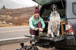© Cavan Images - Portrait of smiling young woman tying shoelace while sitting with dog in trunk of off-road vehicle during winter