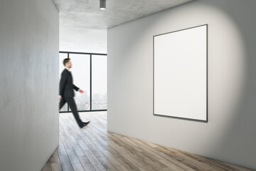 Poster - Businessman walking in modern gallery interior with mock up poster on walls, wooden flooring and window with city view. Museum or apartment concept.