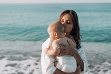 A Young Mother Walks Along The Beach With A Small Child In Diapers. Mother Day. Family With One Child. Happy Childhood With Mommy. Walking Ocean Wave