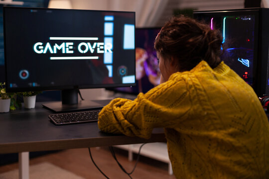 Angry streamer losing space shooter videogames during online entertainment competition at home in living room. Game over on computer screen. Player performing cybersport championship