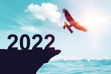 2022 new year concept with eagle bird flying away and holding number 1 on sunset sky background at tropical beach.