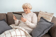 © Yakobchuk Olena - Old woman using digital tablet while relaxing on sofa and reading e book