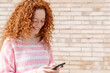 © Westend61 - Cheerful redhead woman text messaging through smart phone in front of wall