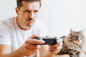 Wall Mural - Concentrated young man with cat playing video game together at home. Close-up portrait of guy gamer player holding wireless gamepad and concentrating on cosole game. Hobby, entertainment industry