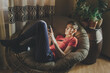 © Kathleen - A young man looks at his smartphone lying in a chair at home