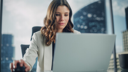 Poster - Portrait of Successful Young Businesswoman Sitting at Her Desk Working on Laptop Computer in Big City Office. Beautiful Social Media Strategy Manager Plan Disruptive e-Commerce Campaign