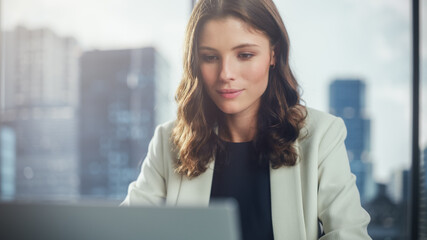 Poster - Portrait of Successful Young Businesswoman Sitting at Her Desk Working on Laptop Computer in Big City Office. Beautiful Social Media Strategy Manager Plan Disruptive e-Commerce Campaign