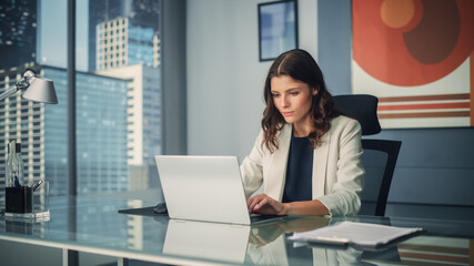Poster - Portrait of Young Successful Caucasian Businesswoman Sitting at Desk Working on Laptop Computer in City Office. Ambitious Corporate Manager Plan Investment Strategy for e-Commerce Project.