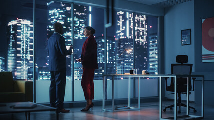 Poster - Successful Corporate Top CEO's Talking, Using Laptop Computer Standing in Big City Office at Night. Two Successful Managers Discuss Environmental, Social, Corporate Governance for e-Commerce Project