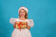Happy little girl in a lush blom dress for a holiday. fun child in Santa hat hold gift Happy merry Christmas. beautiful girl smiles laughs. box gold bow. Happy New Year. Place for text. Copy space. 