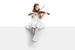 Full length portrait of a girl in a white dress sitting on a blank panel and playing a violin