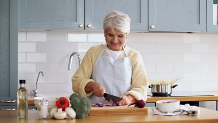 Wall Mural - healthy eating, food cooking and culinary concept - happy smiling senior woman with knife chopping red onion on kitchen