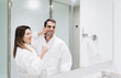 © Westend61 - Smiling woman looking at mirror while applying face cream on man face in hotel bathroom