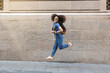 © Westend61 - Happy woman with backpack jumping on footpath in front of wall