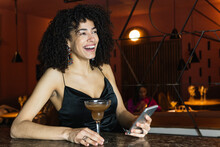 Smiling Woman With Mobile Phone And Drink Looking Away In Restaurant