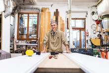 Smiling Mature Craftsperson Standing At Table In Workshop
