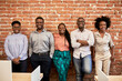 © Westend61 - Smiling male and female professionals standing together in front of brick wall in coworking office