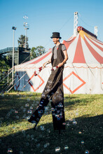 Male Juggler Holding Juggling Pins While Walking With Stilts On Meadow