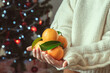 © spass - Child hands in knitted sweater holding fresh mandarins with green leaves with bokeh on background