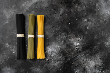 Three colors dry raw pasta, on black dark stone table background, top view flat lay, with copy space for text