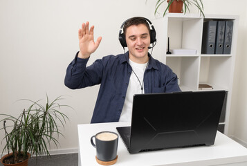 A man in headphones with a microphone sits at a laptop at an online meeting. Remote work concept.