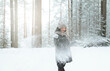 white young woman in a hat and mittens and a black jacket throwing snow in winter in the forest among the trees