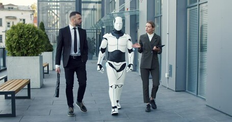 Business man in suit speaking with his female colleague at the street. Woman using tablet computer while managing droid and telling something to her male partner. Innovations and cyber droid concept