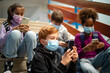 © littlewolf1989 - Group of school children wearing face masks and using smart mobile phones before class.
