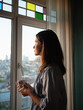 © ZHPH Production/Stocksy - Woman with a coffee looking to the window at evening