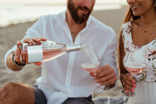 A Couple Drinking Rose Wine On The Beach At Sunset