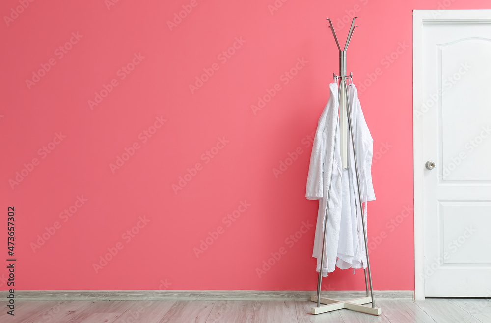 Rack with white bathrobes near pink wall