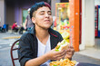 © Ana Luz Crespi/Stocksy - Latino gen z laughing while eating a comfort food