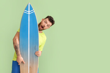 Surprised young bearded man with surfboard on green background