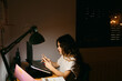 © Eloisa Ramos/Stocksy - Teen girl texting sitting on her desk at night