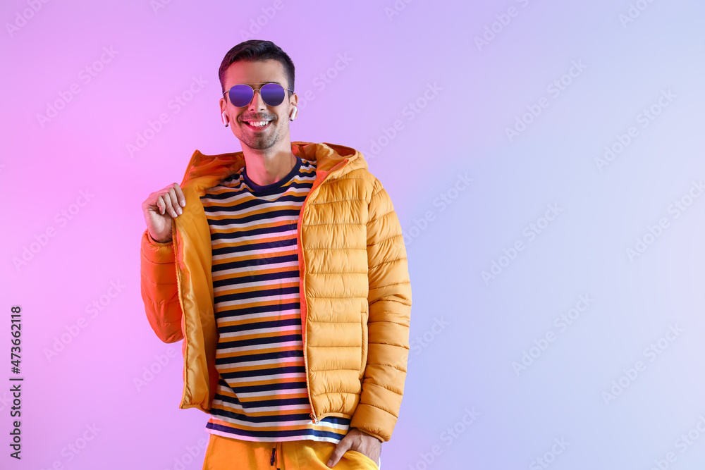 Stylish young man in sunglasses and yellow jacket on color background