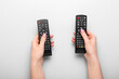 © Pixel-Shot - Female hands with TV remote controllers on grey background