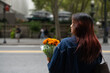 © Lauren Lee/Stocksy - Young woman standing in street with bouquet of flowers