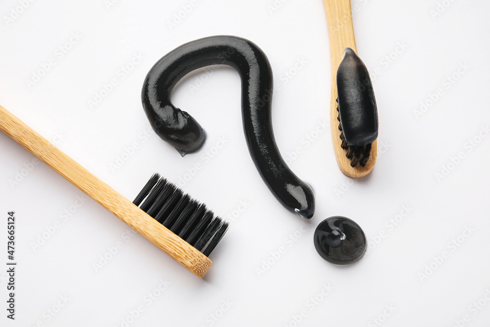 Question mark made of black tooth paste and bamboo brushes on white background