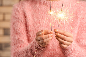 Woman in pink sweater holding Christmas sparklers on brick background, closeup