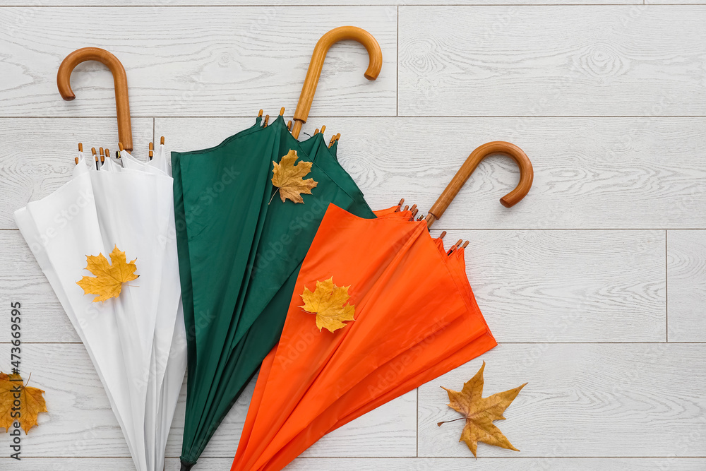 Different umbrellas and autumn leaves on light wooden background