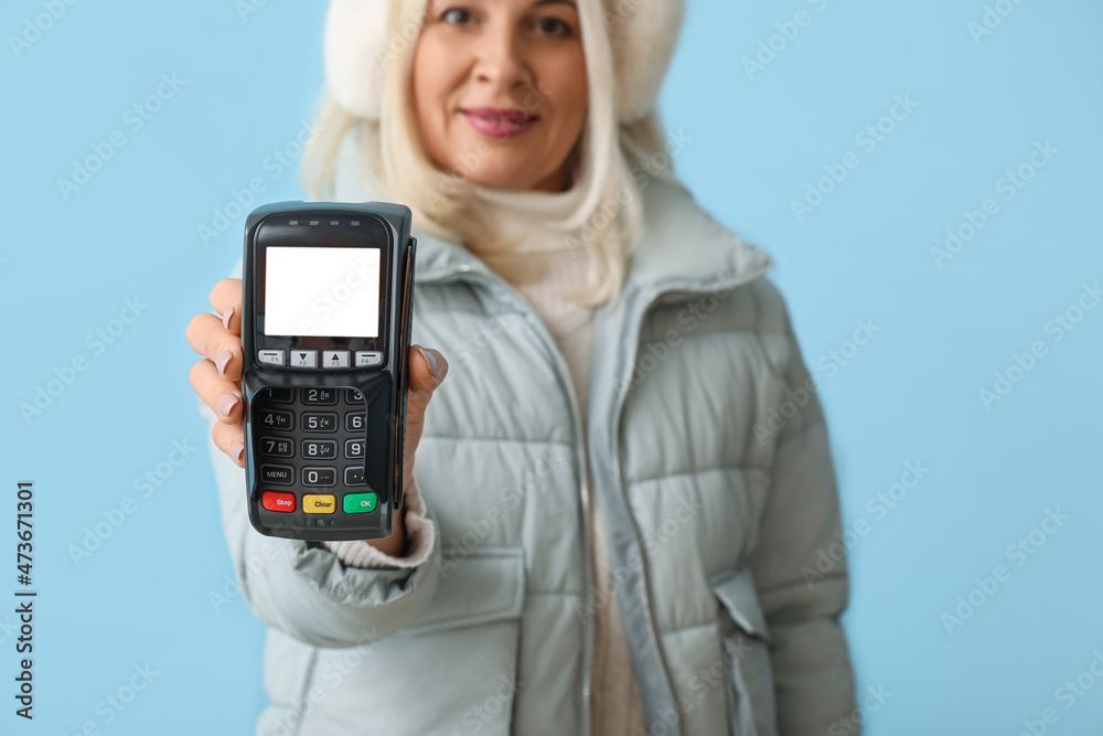 Mature woman with banking terminal on color background