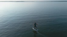 Man Riding On A Hydrofoil Surfboard On Large Blue Lake In Sunny Weather. Aerial Shot Of Man Riding A Hydrofoil Surfboard In The Middle Of Lake. High Quality 4k Footage