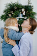 © Sergey Narevskih/Stocksy - Smiling woman with child against Christmas wreath