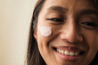 © Anna Tabakova/Stocksy - Smiling east asian model with cream on her face