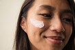 © Anna Tabakova/Stocksy - Smiling east asian model with cream on her face