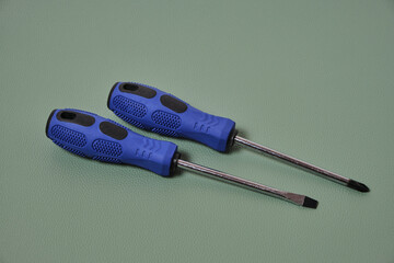 Two screwdrivers cross and flat with blue handles on a green background.