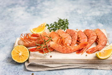 Raw Argentine shrimps on white wooden cutting board with lime, herbs and pepper. Seafood.